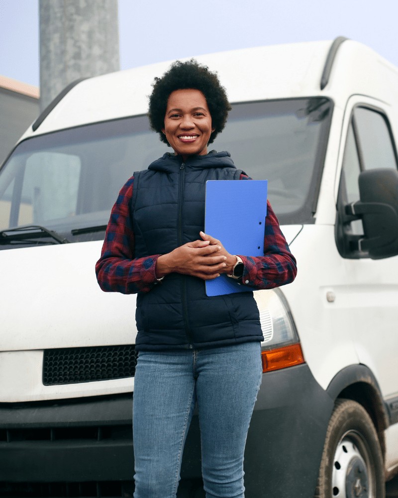 A delivery associate standing route-ready at the front of her van